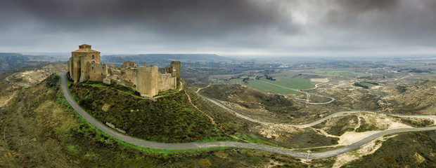 Aerial panorama view of the ruined medieval abandoned Montearagon castle, namesake of the famous kingdom on a bare mountain top near Huesca, Aragon province Spain with stormy cloudy sky