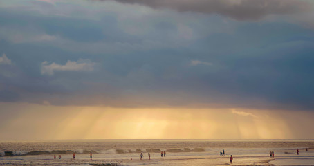 People playing in the sea at sunset with rainfall at a distance 