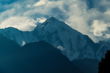 View on Himalayas from Annapurna Circuit Trek, Nepal. Clouds covered with clouds. Sharp slopes. Smaller mountain in front, covered in shadow.  Overcast but sunny. High altitude climbing.