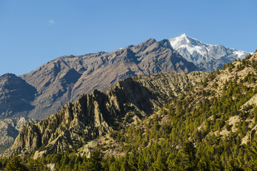 Himalayas Mountain Range, Annapurna Circuit Trek, Nepal. Clear sky above the peak. Slopes covered with large amount of trees. Limestone rocks. Serene landscape. Dangerous mountains