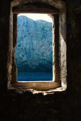 Window in an old stone wall overlooking the sea bay and the mountain.