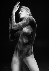 Beautiful slim girl wearing a gymnastic bodysuit covered with white powder talcum dust jumps dances on a dark. Artistic conceptual and advertising black and white photo
