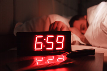 Alarm clock on bedside table with red numbers, kitchen knife, sleeping man in bed in dark room. Concept chef sleeping after hard day at restaurant, sleep disturbance, oversleep work, night shift