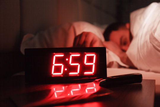 Alarm Clock On Bedside Table With Red Numbers, Kitchen Knife, Sleeping Man In Bed In Dark Room. Concept Chef Sleeping After Hard Day At Restaurant, Sleep Disturbance, Oversleep Work, Night Shift