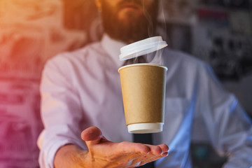 Barista in a white shirt with a tie holds floating in the air a paper cup with a hot drink on his outstretched arms. Barista wizard concept. Background for advertising and placing logo on your drink