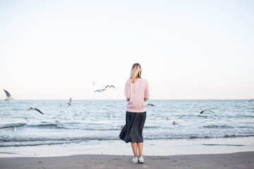 Fototapeta na wymiar A girl stands on the beach and seagulls are flying nearby. Enjoy the moment. Rest and relaxation by the sea. Weekend in nature. Life style