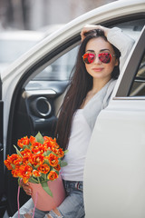 Young attractive woman in the car with presents box, gift and flowers. Beautiful lady in spring time with bouquet of tulips. Female in the automobile. © olenachukhil