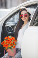 Young attractive woman in the car with presents box, gift and flowers. Beautiful lady in spring time with bouquet of tulips. Female in the automobile. © olenachukhil