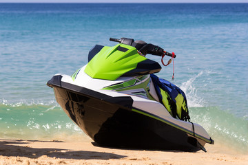A green-white jet ski is on a beach in waves of blue sea in the sunny weather. Active rest is happy...