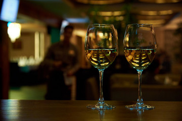 Two glasses of white wine with a reflection on the bar.