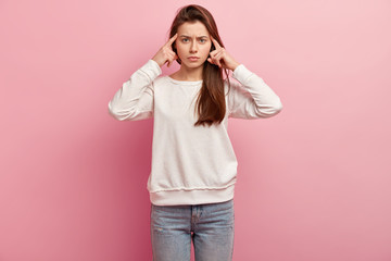 Image of serious European young woman tries to concentrate, keeps fore fingers on temples,...