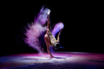 Obraz na płótnie Canvas Slim girl dancing in color dust in the dark