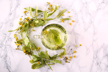 A cup of lime tea on a marble table. Dry leaves of linden leaves next to the cup.