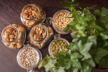 Jars of nuts on a dark table with a plant. Sunflower seeds, pumpkins, cedar, walnut, peanuts, cashews
