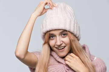 Cropped studio portrait of attractive woman in pink sweater and white hat looking with satisfaction at camera, with a cheerful smile holding her hat, perfect skin/ people, beauty and fashion concept.