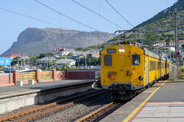 Fototapeta na wymiar Kalk Bay, Cape Town, South Africa. Circa 2017. A yellow metro passenger train at Kalk Bay station
