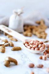 Raw peanuts in a wooden spoon on a marble table. A peanut shell is lying next to a spoon.