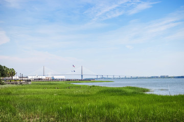 Fototapeta na wymiar Beautiful summer landscape with green grass in the foreground, a bridge in the center and a clear blue sky. The famous bridge in the city of Charleston. Charleston,South Carolina / USA - July 21, 2018