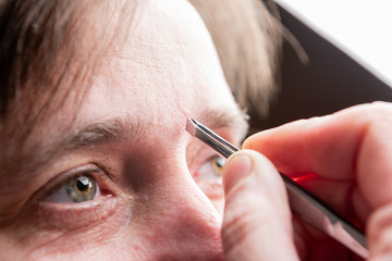Woman plucking eyebrows with tweezers in home.