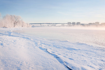 Obraz premium Winter landscape in the early morning overlooking the city of Dubna and the bridge over the Volga. Frosty fog obscures the banks of the river. The tops of the trees are covered with hoarfrost.
