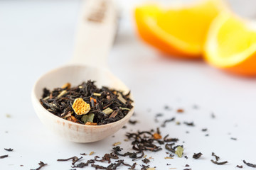 A wooden spoon with dry leaves of black tea with orange peel on the table.