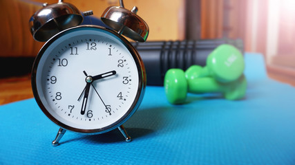 Blue yoga mat, two dumbbells, alarm clock, self-massage roll - time for sport