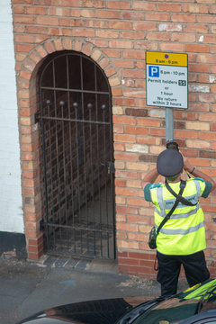 Traffic Warden Or Civil Enforcement Officer Putting Ticket On Black Car In UK