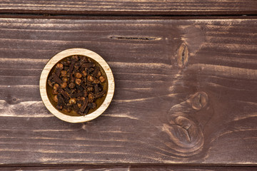 Lot of whole small dried cloves spice with wooden bowl flatlay on brown wood