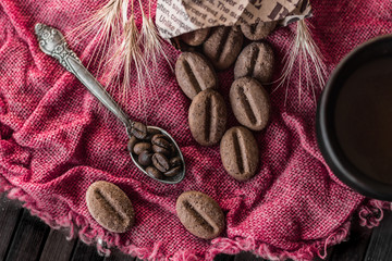 Coffee beans in a spoon and biscuits in the form of coffee beans are scattered on a linen napkin. Close-up. Bright background. View from above.
