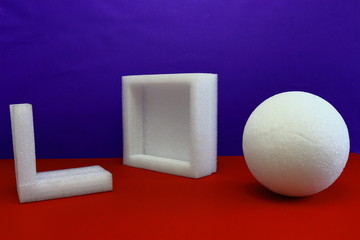 A color image of styrofoam shapes on a red table with a purple background.