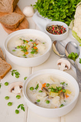 Cheese cream soup with cauliflower, mushrooms and green peas in a bowl on a white wooden background.