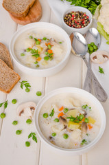 Cheese cream soup with cauliflower, mushrooms and green peas in a bowl on a white wooden background.