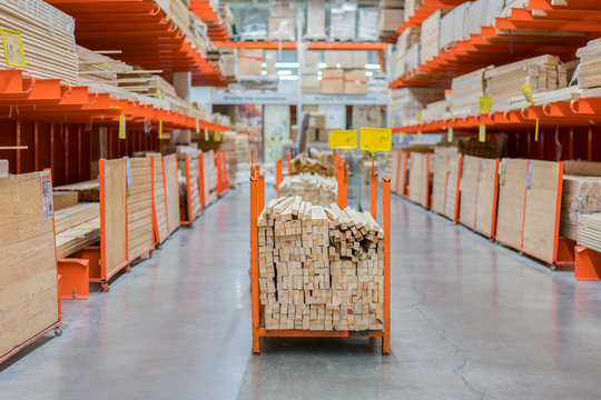 Stack New Wooden Bars On Shelves Inside Lumber Yard Of Large Hardware Store In America. Rack Of Fresh Mill Or Cut Wood Timber With Flatbed Cart And Manual Forklift In Warehouse.