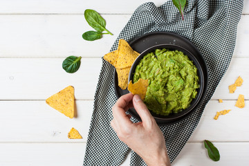 Guacamole freshly cooked in a bowl, overhead view on man hand is picking some guacamole dip with chip