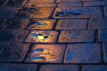 Wet cobblestones in the dusk, lamp reflecting in the water