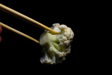 Cauliflower taken with Chinese chopsticks. Vegetarian food. Cauliflower on a dark background.
