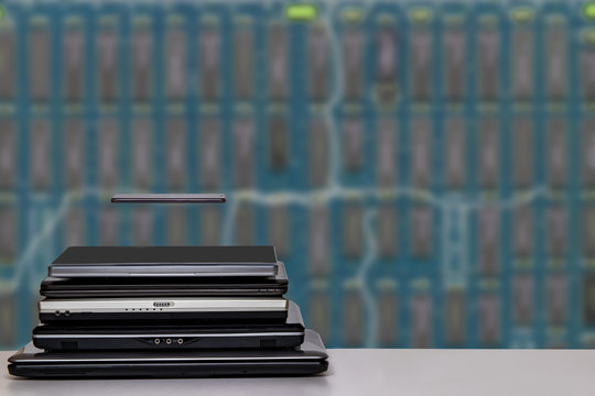 Stack of laptop computers and a smartphone. A pile of computers and a smartphone on a bright table against bright blurred blue digital electronic circuit board texture background. PCB. - Powered by Adobe