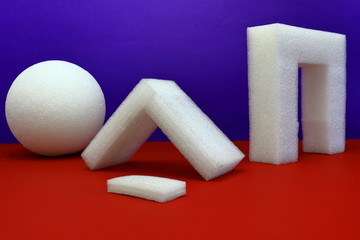 A color image of styrofoam shapes on a red table with a purple background.