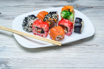 Sushi on a white plate on a light wooden background.