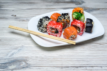 Sushi on a white plate on a light wooden background.