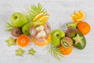 Summer cocktail with various tropical fruits around. Apple, kiwi, tangerine, orange, mango, carambola.