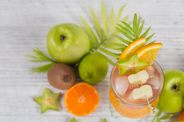 Summer cocktail with various tropical fruits around. Apple, kiwi, tangerine, orange, mango, carambola.