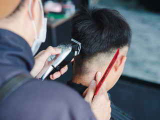 Close up barber using hair clipper and comb to cut the hair in the barber shop.