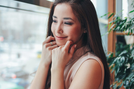 Portrait of beautiful charming romantic brunette smiling asian girl near the window at cafe