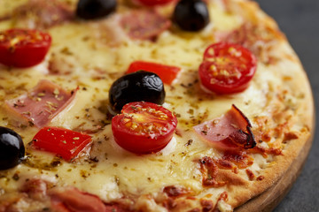 Pizza with ham, mozzarella cheese, cherry tomatoes, red pepper, black olives and oregano. Home made food. Concept for a tasty and hearty meal. Black stone background. Close up.