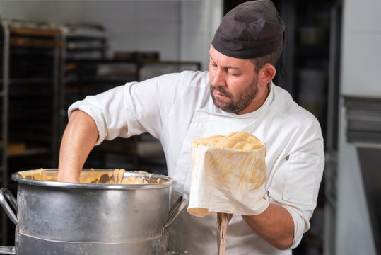Pastry cheff filling the pastry bag with whipped cream at pastry shop's kitchen .
