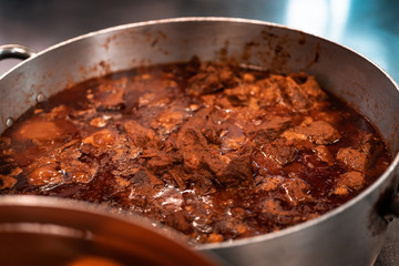Traditional Goulash and mexican stew mix, slow coking style in big steel pan. Chicken and gravy preparation. Hot meal for local homeless people. Poverty and nutrition concept, food politics.