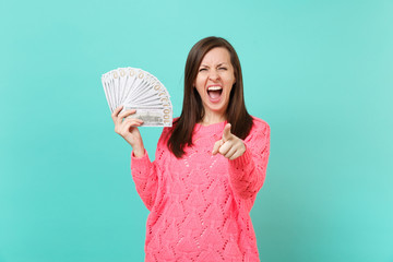 Crazy young woman in pink sweater screaming, pointing index finger on camera hold lots bunch of...