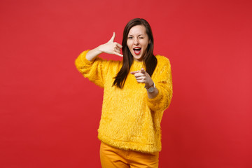 Fototapeta premium Stunning young woman blinking, pointing index finger on camera, doing phone gesture like says call me back isolated on red background. People sincere emotions, lifestyle concept. Mock up copy space.