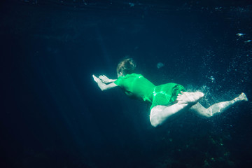short-haired girl in a green dress swims underwater in the sea